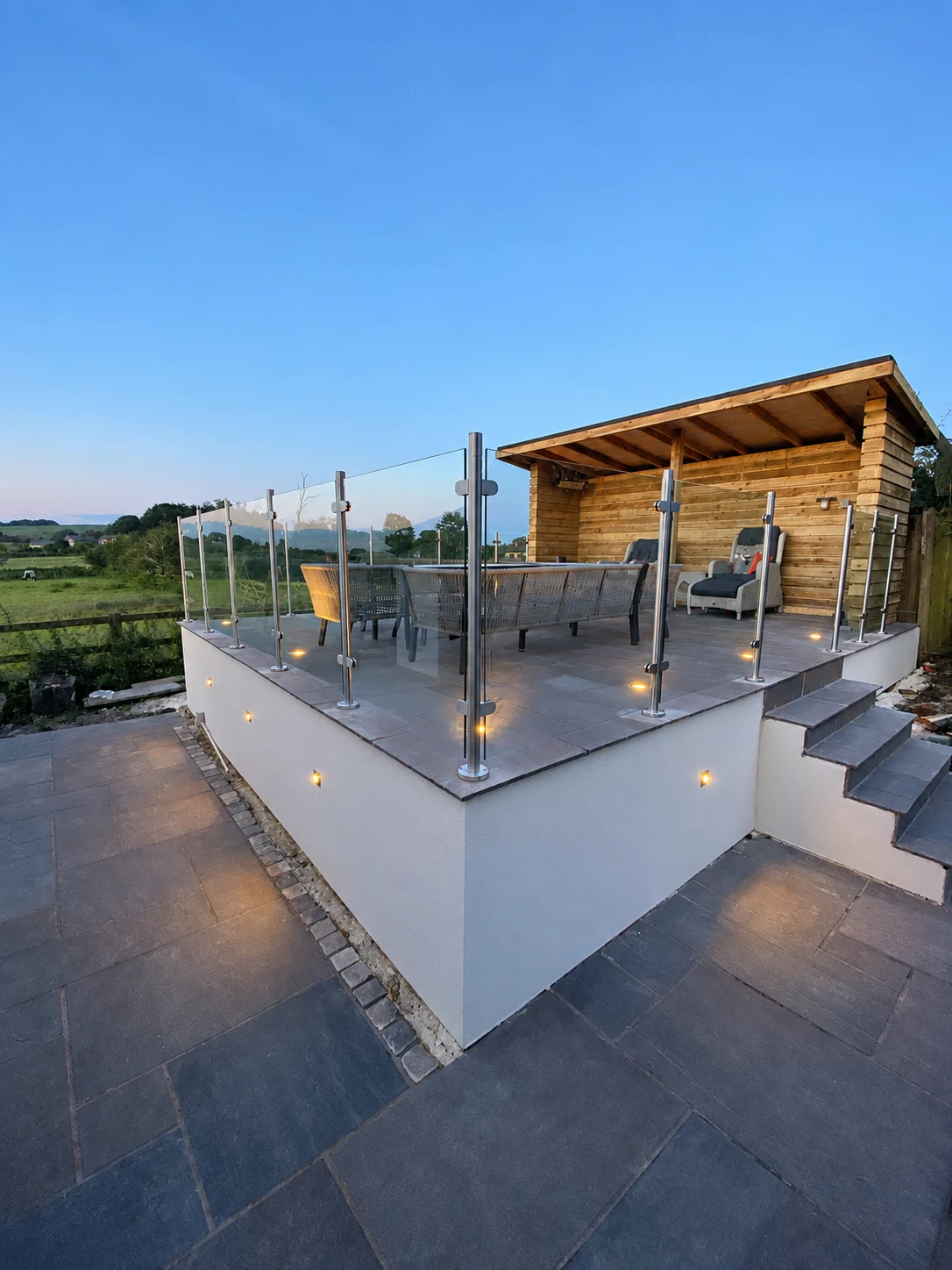 The Terrace in Brinscall with glass balustrades, stone paving, timber shelter and evening lighting